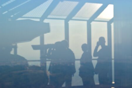 Silhouette of a people watching through telescope on observation tower; Landscape is visible in the backgroundの写真素材