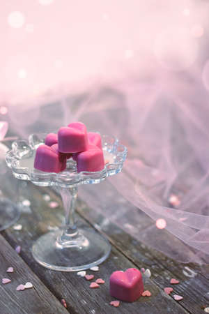 Pink chocolate pralines in heart shape, in beautiful glass bell, on white wooden background with ...