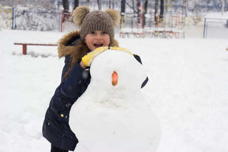 Little girl having fun, making snowman; winter background with copy space