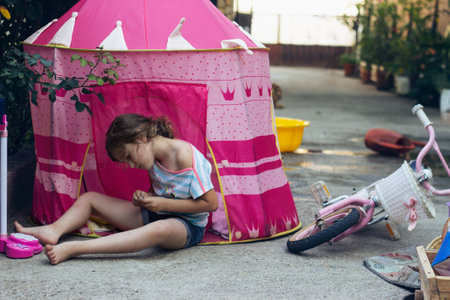 Little girl sitting in backyard, playing in tent;の写真素材