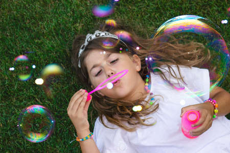 Top view of a beautiful little girl laying on the grass, blowing soap bubblesの写真素材
