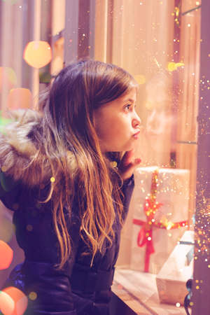 Beautiful little girl in front of confectionery shop, decorated with wrapped gift boxes and candies....
