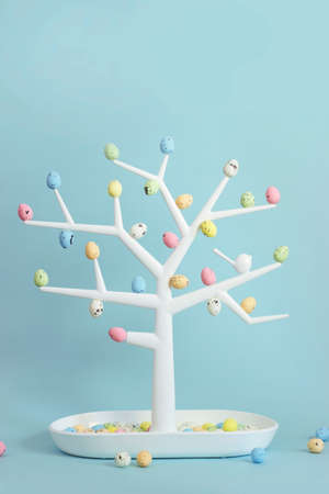Small decorative tree with colorful quail eggs on branches; Easter background with copy space