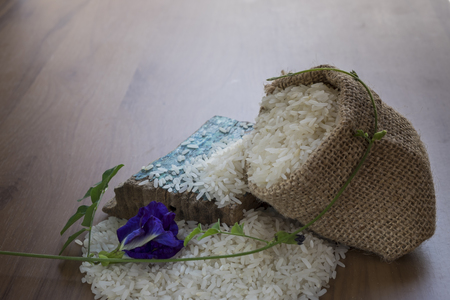 Brown rice in sack and pea flowers on wooden backgroundの写真素材