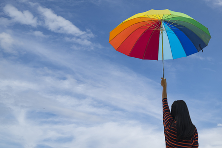 Young woman holding colorful umbrella on blue sky. Summer Vacation Concept.の写真素材