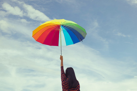 Young woman holding colorful umbrella on blue sky. Summer Vacation Concept. Filtered image processed vintage effect.の写真素材