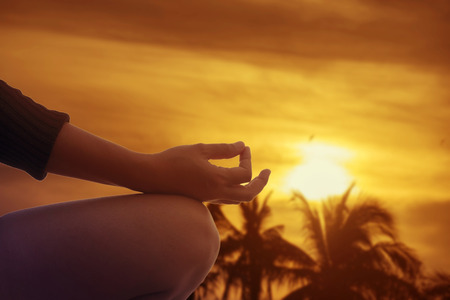 hand of a woman meditating in a yoga pose on the beach at sunsetの写真素材