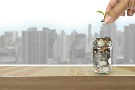 Hand putting money coins and seed in clear bottle on photo blurred cityscape background,Business investment growth conceptの写真素材