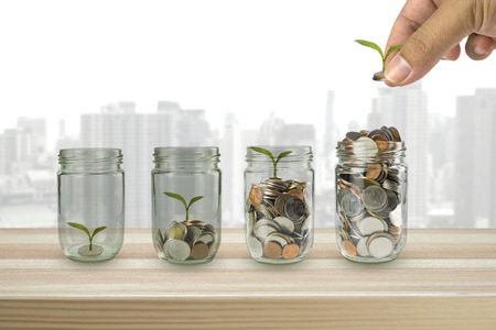 Hand putting money coins and seed in clear bottle on photo blurred cityscape background,Business investment growth conceptの写真素材