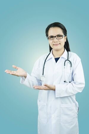 Female doctor with stethoscope show something  on blue background, medicine and health care conceptの写真素材