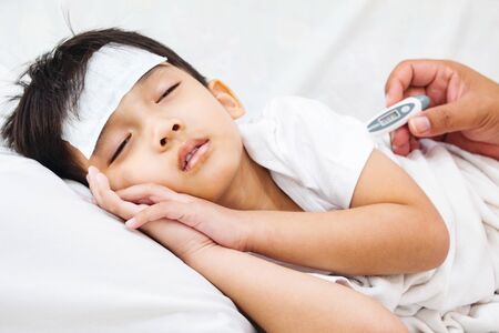 Asian boy is not comfortable. The gel attach to the gel cooling pad on his head for relief the fever.の写真素材