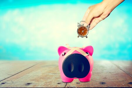 Hand with Alarm Clock in piggy bank on blurred  backgroundの写真素材