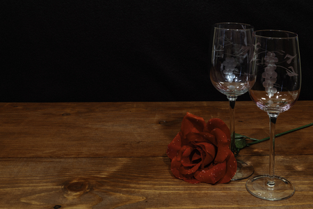 Beautiful etched wine glasses with a single red rose on wooden table and dark background. Valentines, Mothers Day, Easter, Christmas, Wedding Conceptsの写真素材