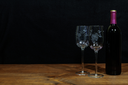 Beautiful etched wine glasses and bottle of red wine on wooden table and dark background. Valentines, Mothers Day, Easter, Christmas, Wedding Conceptsの写真素材