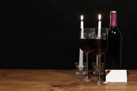 Beautiful etched wine glasses and bottle of red wine, white candles, on wooden table with name tag on dark background. Valentines, Mothers Day, Easter, Christmas, Wedding Conceptsの写真素材
