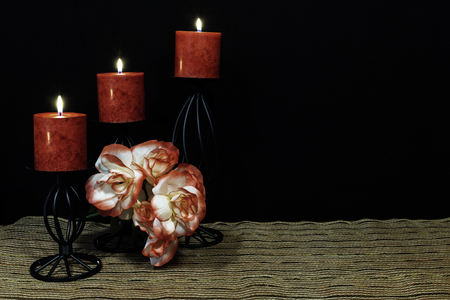 Beautiful orange and white roses, red candle perched on black candle holders on mesh place mat and wooden table with dark background. Valentines, Mothers Day, Easter, Christmas, Wedding Conceptsの写真素材