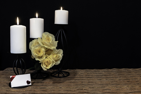 Beautiful bouquie of yellow roses, white candles perched on black candle holders on mesh place mat and wooden table with card and dark background. Valentines, Mothers Day, Easter, Christmas, Wedding Conceptsの写真素材