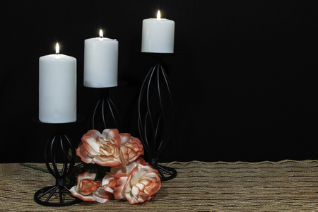 Beautiful orange and white roses, white candle perched on black candle holders on mesh place mat and wooden table with dark background. Valentines, Mothers Day, Easter, Christmas, Wedding Conceptsの写真素材