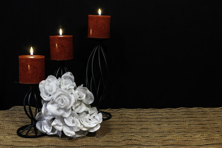 Beautiful bouquie of white roses, red candles perched on black candle holders on mesh place mat and wooden table with card and dark background. Valentines, Mothers Day, Easter, Christmas, Wedding Conceptsの写真素材