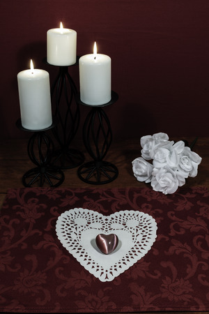 Heart shapped dollie and gemstone, three white candles in metal holoders and bouquet of white roses on wooden table.の写真素材