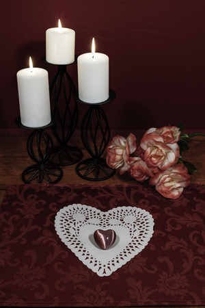 Heart shapped dollie and gemstone, three white candles in metal holoders and bouquet of orange and white roses on wooden table.の写真素材