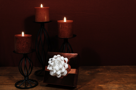 Three red candles in metal holoders and red rose, present with white bow on wooden table.の写真素材