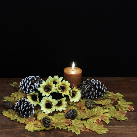 Silk maple leaves, beautiful bouquet of sunflowers, frosted pinecones and orange candle on tabletop with dark background.の写真素材