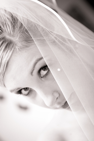 beautiful bride with cute face is directly looking in the cam while the veil is hiding a part of her face  cute eyes in this black and white photoの写真素材