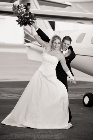 black and white wedding photo from a very young couple at the airport with airplane in background while holding the bouquet and waggle with the armsの写真素材