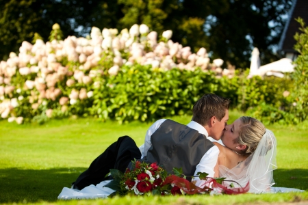just married young wedding couple is laying down on the green meadow in fresh gras with nice colorful flowers in the backgroundの写真素材