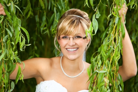 pretty nice bride with glasses eyeglasses is holding at a weeping willowの写真素材