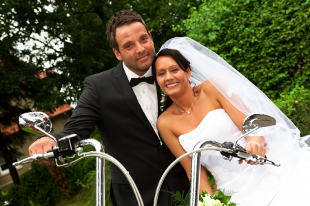 white Bride with veil and groom with bow tie are sitting on motorcycle after wedding ceremonyの写真素材