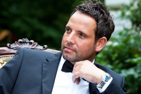 Dark haired handsome groom with bow tie is waiting for his bride and looking around の写真素材