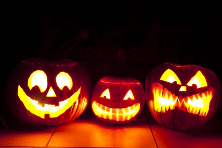 one friendly and two scary pumpkin are shining in scary light in the dark room  three pumpkins on the floorの写真素材