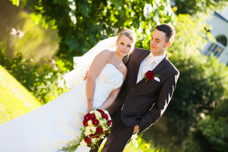 Just married couple is goodlooking. Young couple just married. groom and pretty bride are looking to eachother after the wedding ceremony. she is blond and wearing a nice diadem. foreground and background red roses yellow roses and some greeneryの写真素材