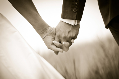 sepia photo with detail of fresh married couple hold hands while walking in a fieldの写真素材
