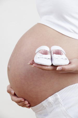 Close Up Of Pregnant Woman Holding Baby Shoesの写真素材