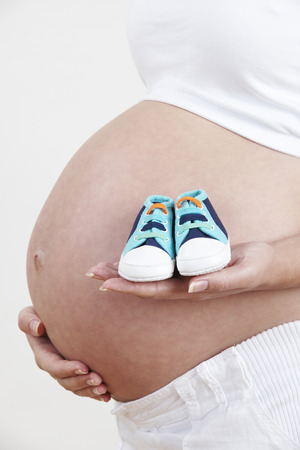 Close Up Of Pregnant Woman Holding Baby Shoesの写真素材