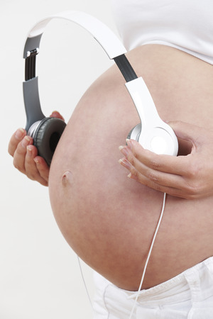 Close Up Of Pregnant Woman Holding Headphones Over Bellyの写真素材
