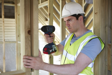 Construction Worker Using Cordless Drill On House Buildの写真素材
