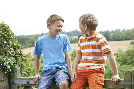 Two Boys Sitting On Gate Chatting Togetherの写真素材