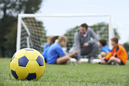 Coach  And Team Discussing Soccer Tactics With Ball In Foreground