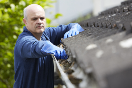 Man Clearing Leaves From Guttering Of Houseの写真素材