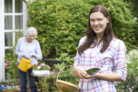 Teenage Granddaughter Helping Grandmother In Gardenの写真素材