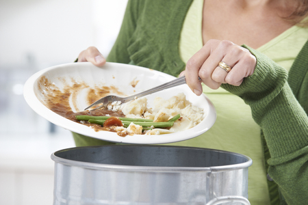 Woman Scraping Food Leftovers Into Garbage Bin Woman Scraping Food Leftovers Into Garbage Bin