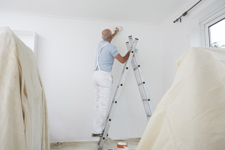 Man On Ladder Decorating Domestic Room With Paint Brushの写真素材