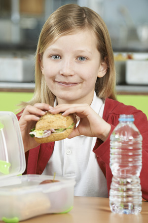 Girl Sitting At Table In School Cafeteria Eating Healthy Packed Lunchの写真素材