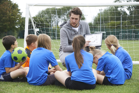 Coach Giving Team Talk To Elementary School Soccer Team