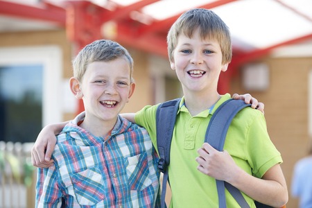 Two Boys Standing Outside School With Book Bagsの写真素材