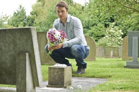 Man Placing Flowers By Headstone In Cemeteryの写真素材